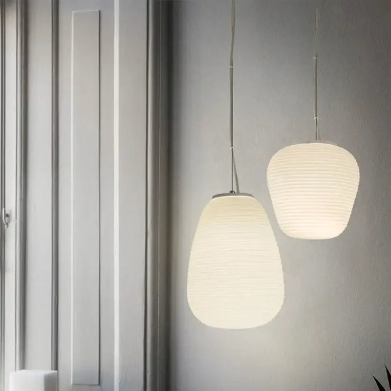 Two off-white ribbed paper decorbites glass cocoon pendant lights hang with slender metal chains against a gray wall