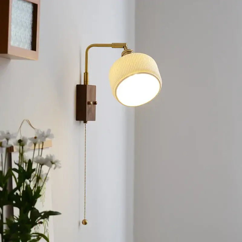 A warm-toned brass led wall lamp with a wooden base and ribbed off-white fabric shade for bedroom mirror lighting