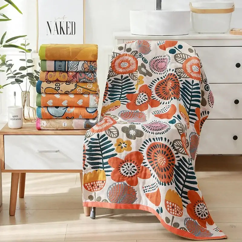 A vibrant orange and teal floral-patterned cotton bath towel with a white base draped over a chair back