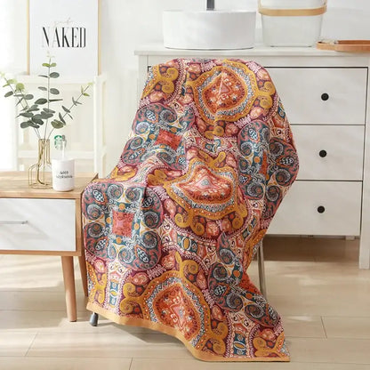 A vibrant throw blanket with paisley motifs in warm orange red and gold tones complements a cotton bath towel decor