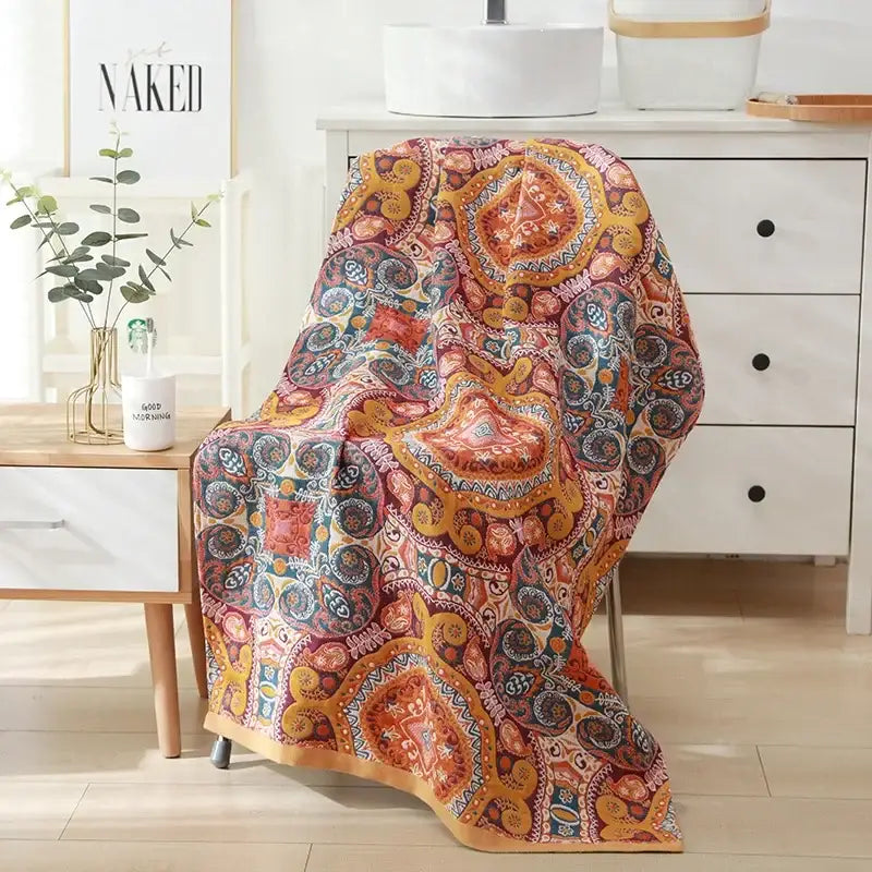 A vibrant throw blanket with paisley motifs in warm orange red and gold tones complements a cotton bath towel decor