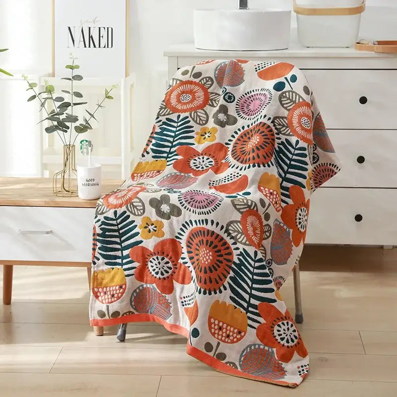 A cozy cream-colored cotton bath towel with vibrant orange teal and yellow floral pattern draped over a chair