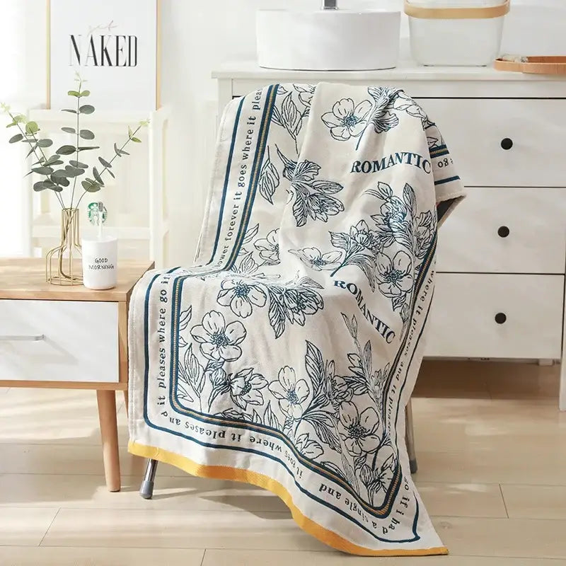 A cream-colored cotton bath towel with blue floral pattern and romantic print draped over a chair for bathroom decor