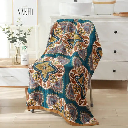 Teal and gold patterned quilted throw blanket with intricate mandala designs paired with beige black floral cotton bath towel for bathroom decor