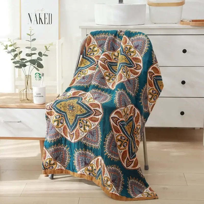 Teal and gold patterned quilted throw blanket with intricate mandala designs paired with beige black floral cotton bath towel for bathroom decor