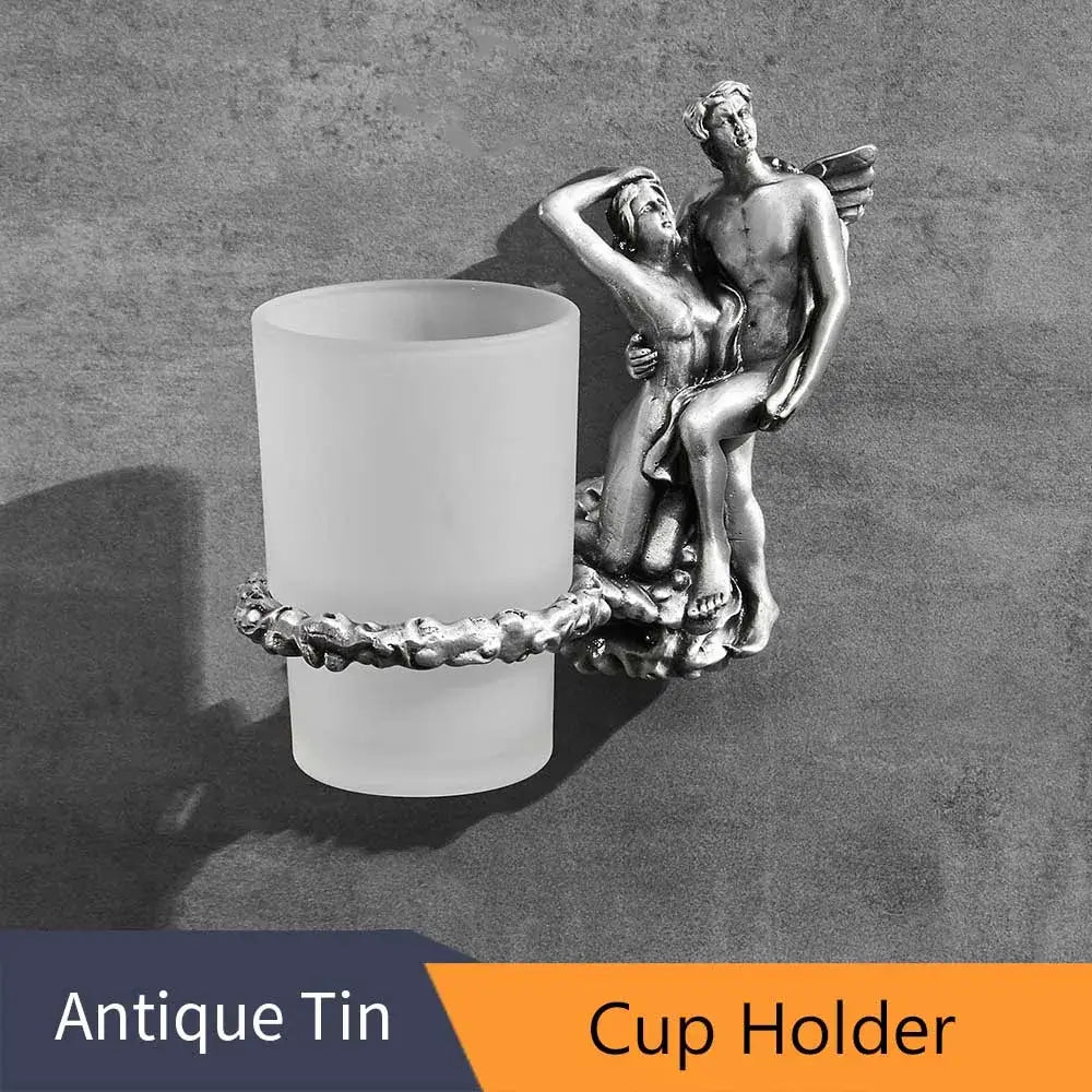 Silver-toned figurine cup holder with sculpted angel and woman design holding frosted glass tumbler in bathroom hardware set