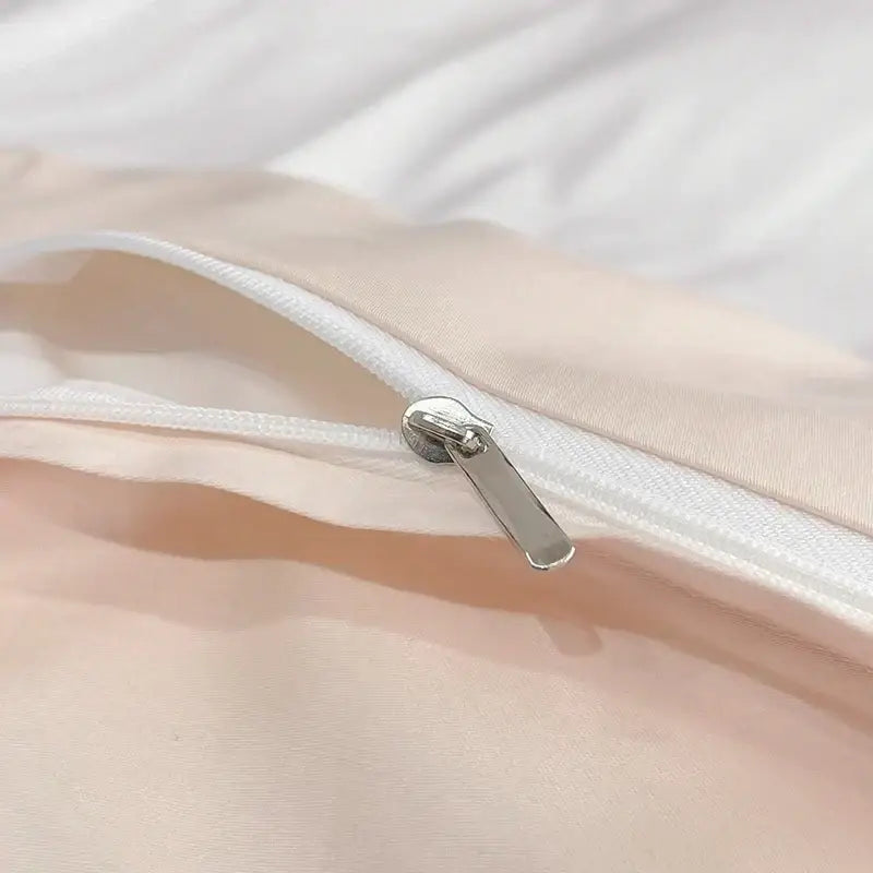 A sleek silver zipper with a metallic pull tab on the seam of soft peach fabric in an embroidered flowers butterfly bedding set