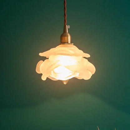 A warm cream-colored ceramic pendant lamp with delicate floral design and brass hardware featuring frosted white glass