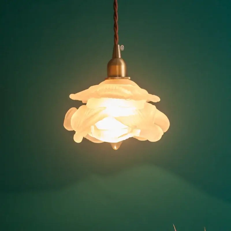 A warm cream-colored ceramic pendant lamp with delicate floral design and brass hardware featuring frosted white glass