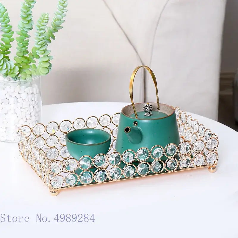 Teal ceramic tea set with gold handles on a crystal-encrusted metal tray beside a rose gold crystal glass mirror tissue box holder