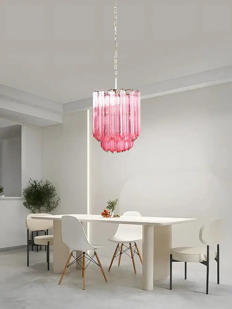 A vibrant rose gold pink glass chandelier with cascading cylindrical shades hangs above the dining table