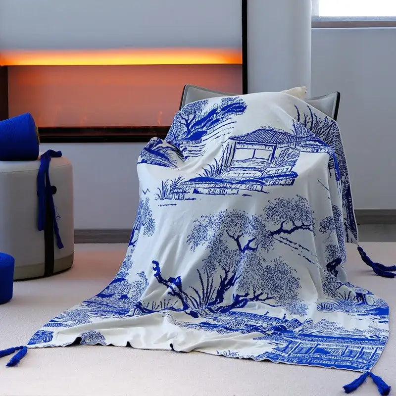 Royal blue and white knitted sofa blanket with intricate blue porcelain-style patterns and tassels at the corners