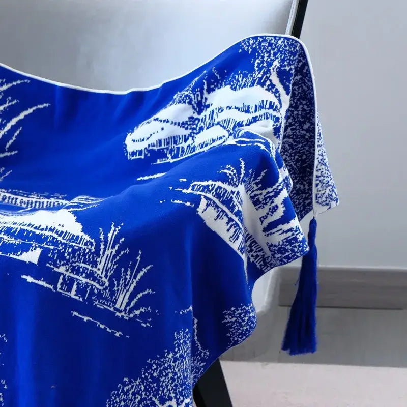 A vibrant royal blue and white knitted sofa blanket featuring a silk scarf design with mountain and tree motifs