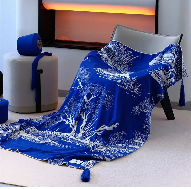 A vibrant royal blue and white knitted sofa blanket with intricate landscape patterns and tassels for living room use