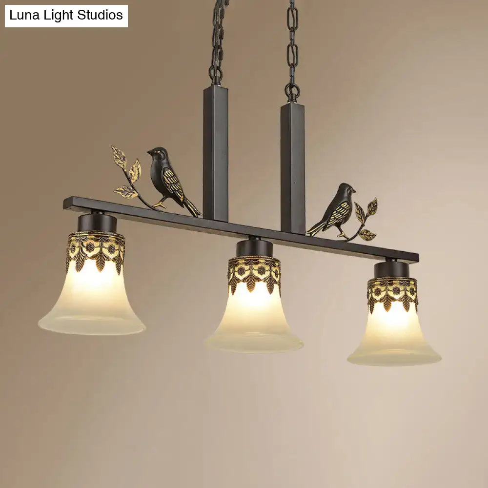 Black metal island light fixture with ornate gold leaf detailing and three frosted glass shades for dining room