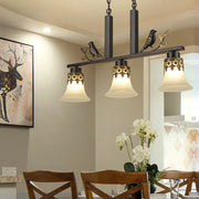 Black wrought iron island light fixture with ornate gold leaf detailing and three frosted glass bell shades