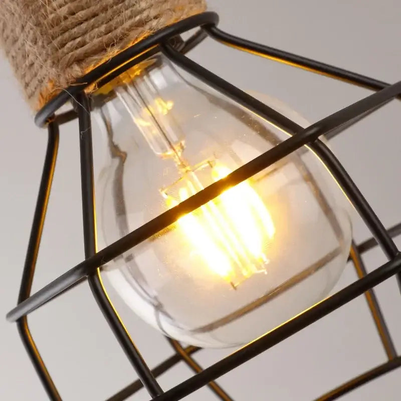 Rustic black iron pendant light with warm edison bulb encased in metal cage and hemp rope cord for dining room use