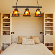 Rustic black metal pendant light with three amber backlit triangular glass shades and deer silhouette scene for dining room