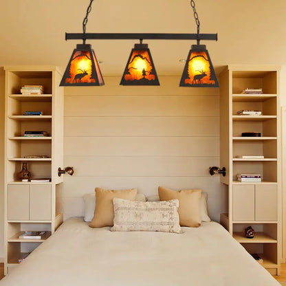 Rustic black metal pendant light with three amber backlit triangular glass shades and deer silhouette scene for dining room