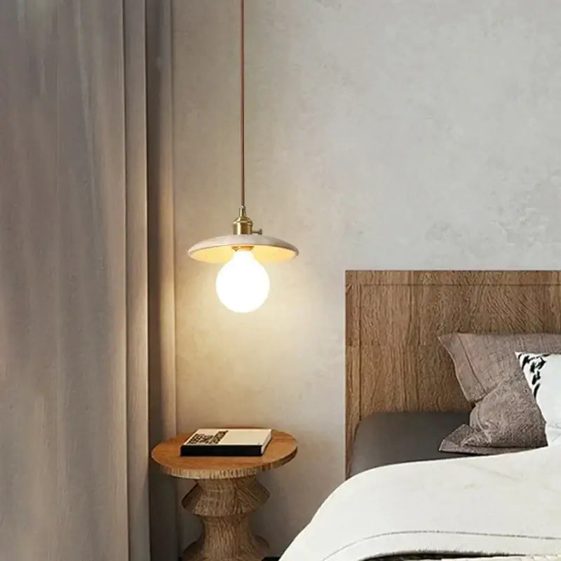 Rustic brass and ceramic glass ball led pendant light with warm-toned brass fixture and white disc shade above wooden nightstand