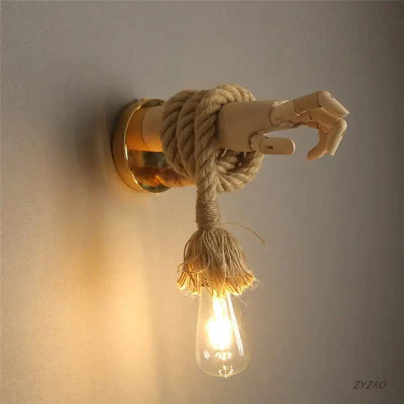 Rustic brass hand shape wall lamp with wooden articulated hand and hemp rope holding exposed filament bulb wall light