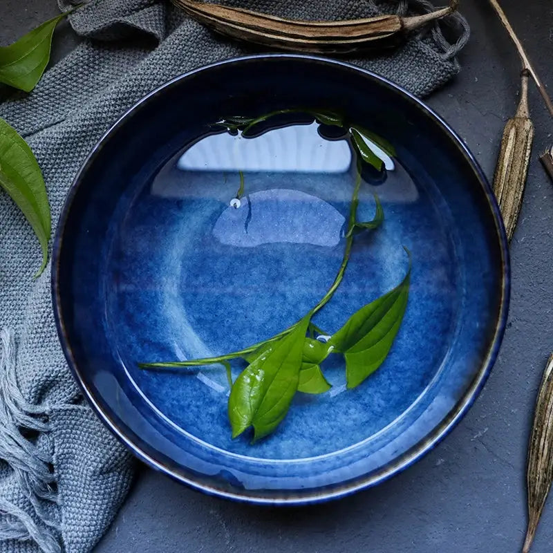 Rustic deep blue ceramic salad bowl with glossy glaze holding clear water and floating green leaves decorbites deep blue porcelain