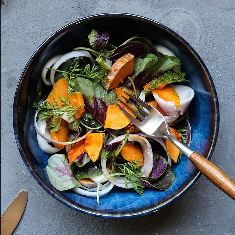 Rustic deep blue ceramic porcelain salad bowl filled with sweet potato salad and fresh dill with wooden fork dining decorbites