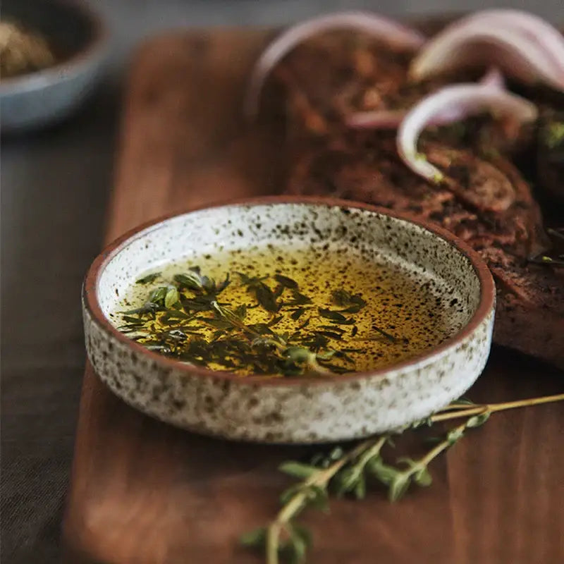 Rustic earthy decorbites ceramic round sauce dish filled with golden olive oil and fresh green herbs