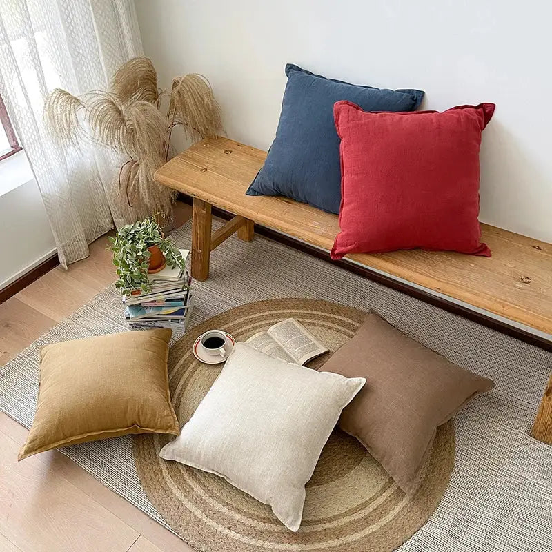 A cozy arrangement of rustic earthy tones linen fringed pillow covers in deep red navy blue beige and tan on a wooden bench