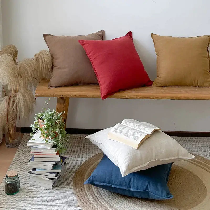 A cozy stack of decorbites linen fringed pillow covers in earthy tones on a rustic wooden bench for living room decor