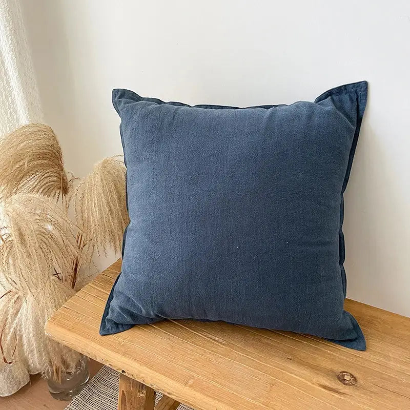 A soft navy blue decorbites linen fringed pillow cover with textured fabric and folded corners on a wooden bench