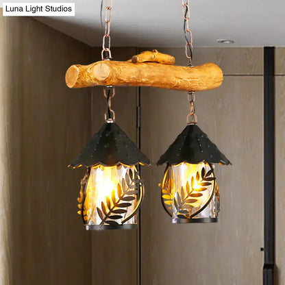 Rustic wooden branch pendant light with two black metal leaf-patterned lanterns and white fabric clear glass shade for farmhouse lighting