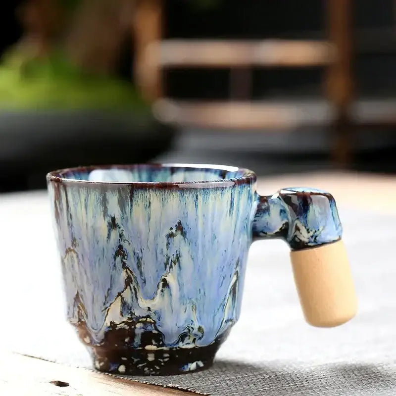 Rustic ceramic latte mug with blue and white glaze mountain patterns and light wood handle for kitchen drinkware