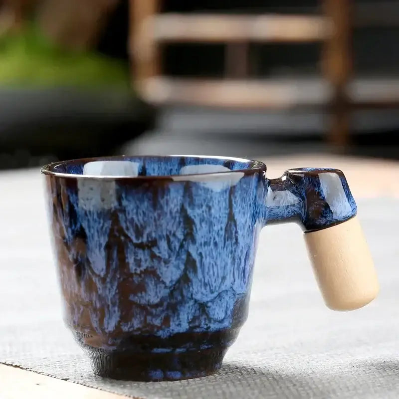 Rustic ceramic latte mug with glossy deep blue glaze, swirling brown patterns, and a light wooden handle