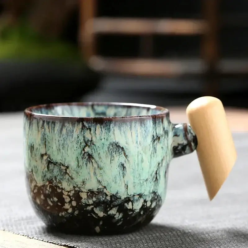 Rustic glazed ceramic latte mug with mottled green and brown finish and smooth wooden handle for kitchen use