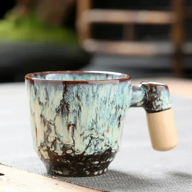 Rustic glazed ceramic latte mug with teal cream and dark brown mottled finish and wooden handle for kitchen drinkware