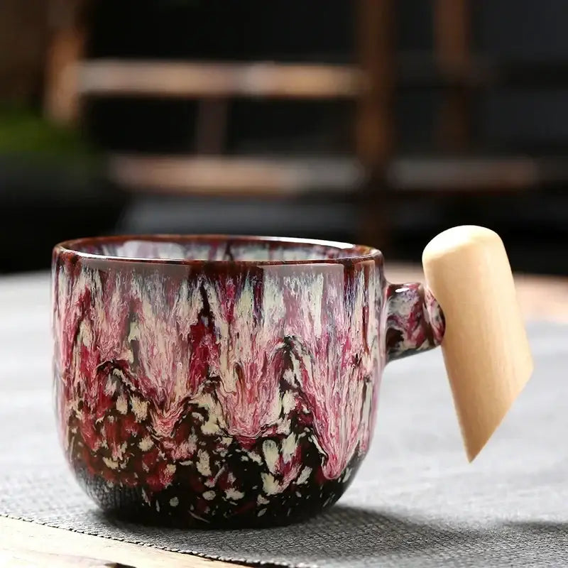 Rustic ceramic latte mug with marbled red white and dark brown glaze and light wood handle for kitchen use