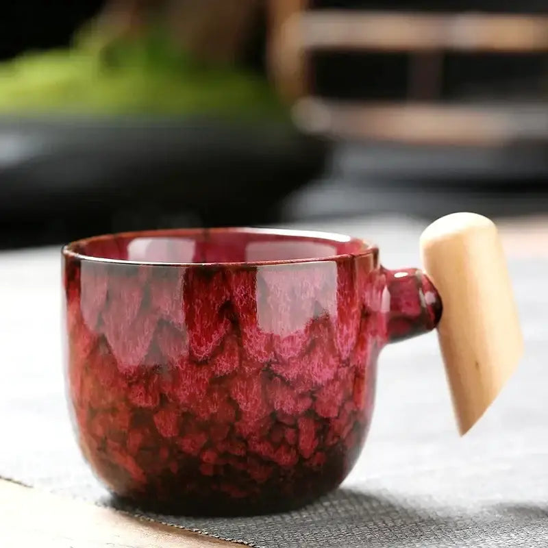 Glossy red rustic glazed ceramic latte mug with textured gradient glaze and light wooden handle for kitchen use