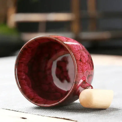 A glossy crimson ceramic latte mug with textured swirling glaze and a smooth wooden handle for rustic drinkware
