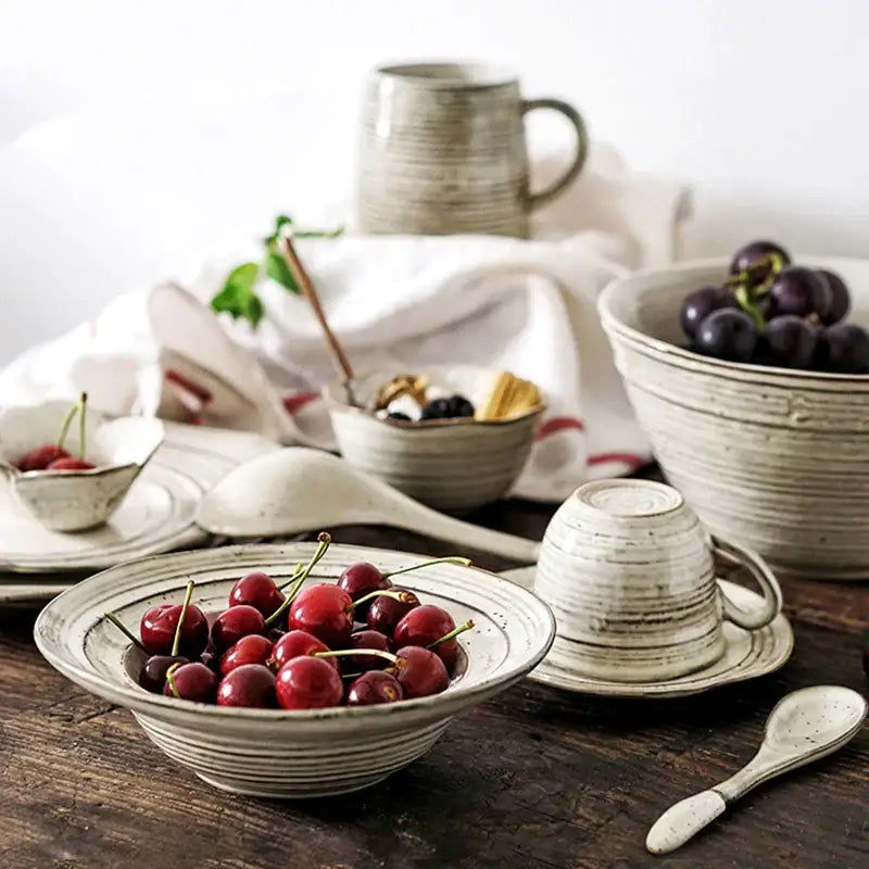 Rustic grayish white ceramic dish bowl set featuring a bowl with horizontal ridges holding vibrant red cherries