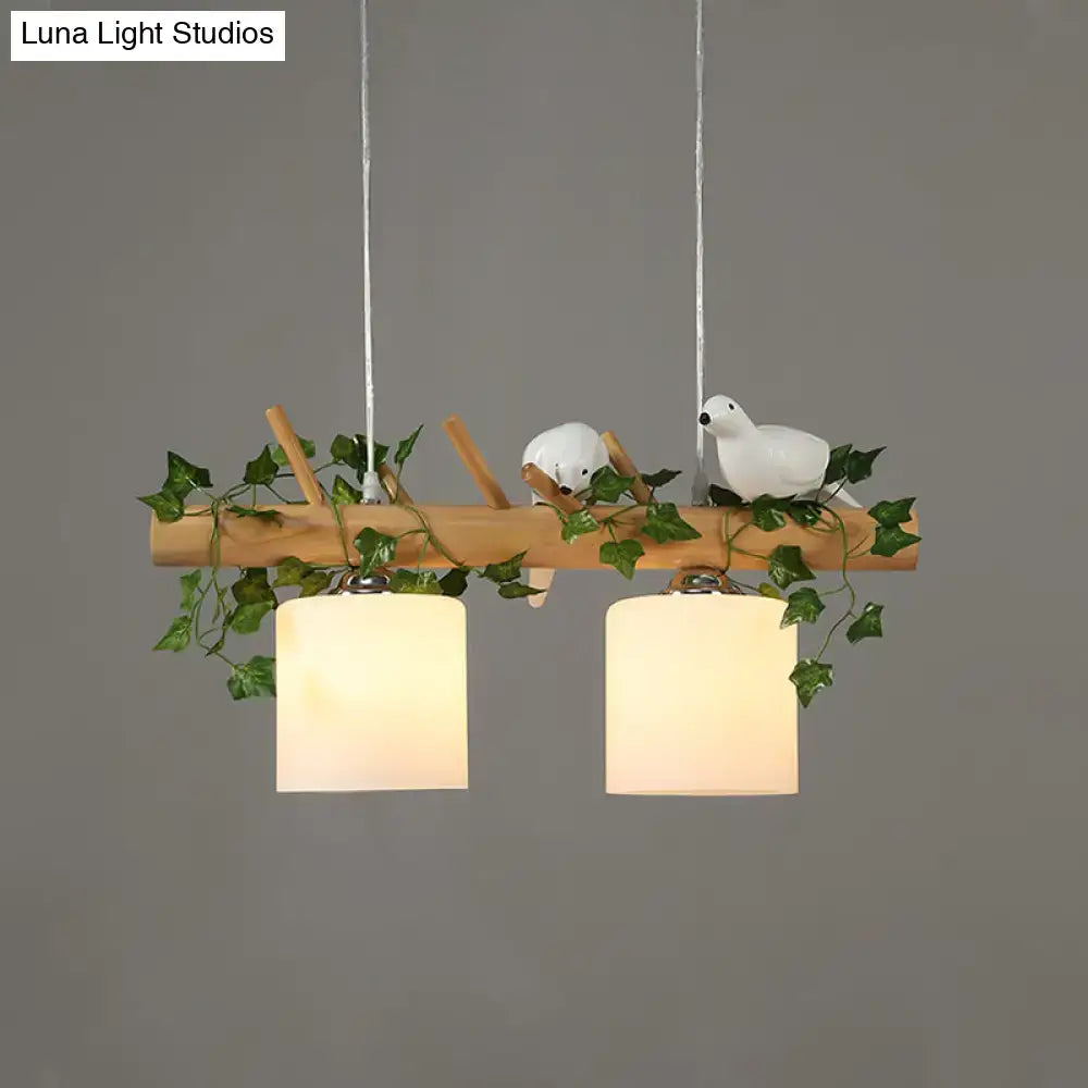 A rustic wooden island pendant light with two cream glass shades adorned with maple green leaf and ceramic birds