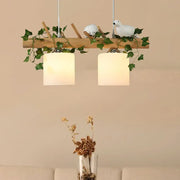 Rustic wooden pendant light with ivory glass shades featuring maple green leaf and white ceramic bird decor