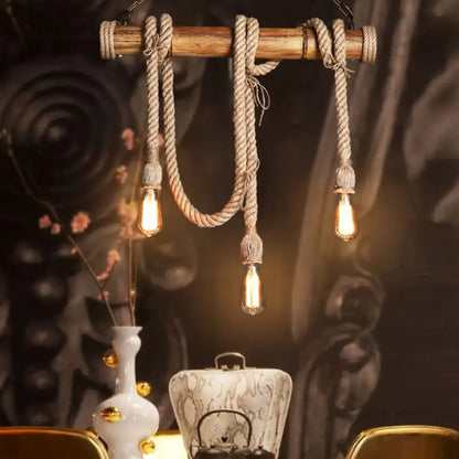 Rustic wooden beam island light with thick beige rope, bamboo accents, and three exposed filament bulbs by decorbites