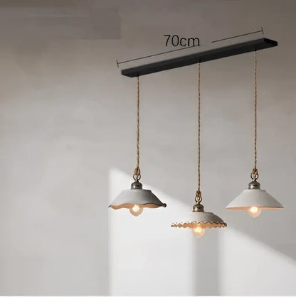 Industrial-style pendant light with matte black bar, brass chains, and off-white ceramic shades in cement loft style decorbites