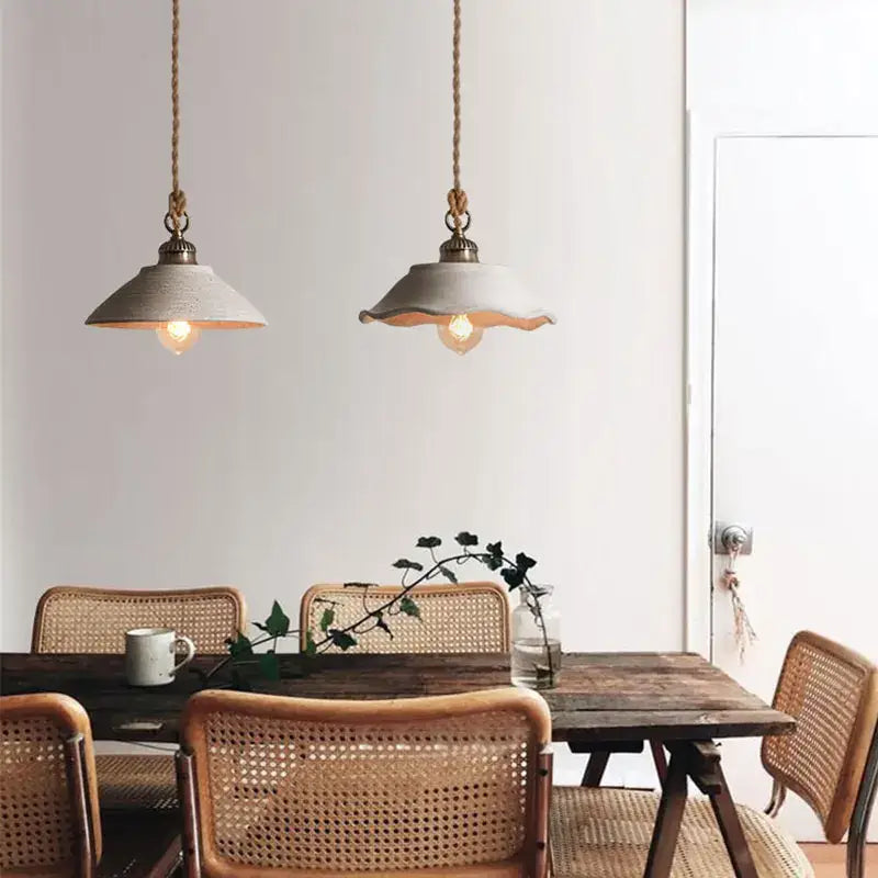 Two rustic off white ceramic pendant lights with brass accents hang from twisted rope cords in cement loft style decorbites