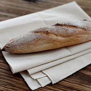 Golden-brown baguette on rustic off-white decorbites linen flax cloth baking mat with a dusting of flour and cracked crust
