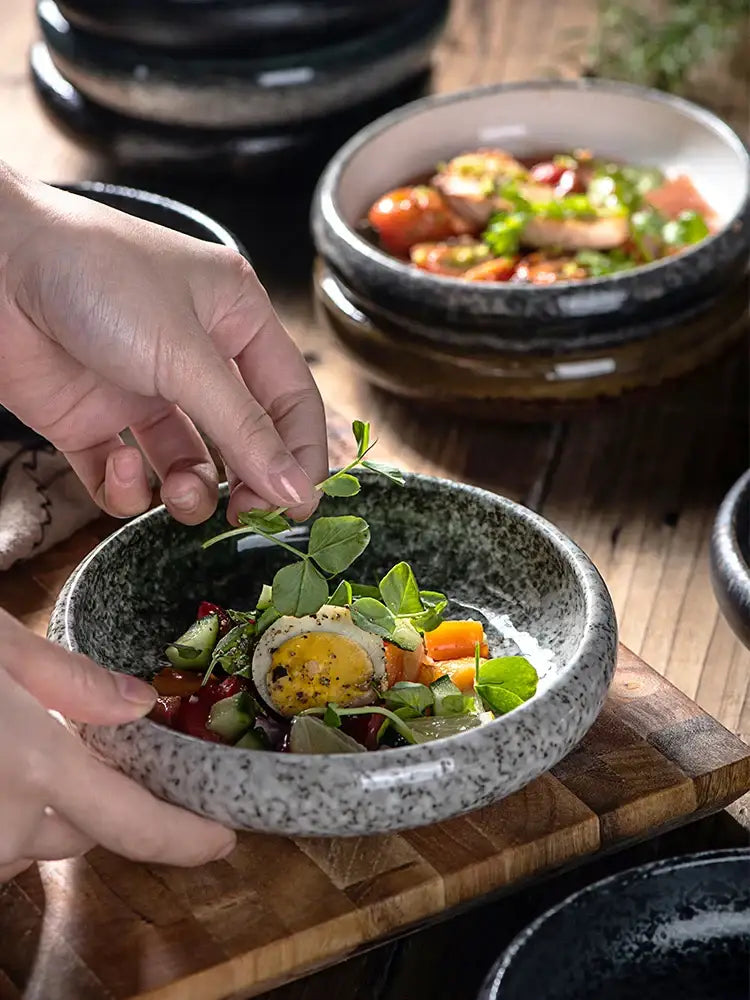 Rustic speckled white and black ceramic kimchi plate holds a vibrant salad with fresh herbs and halved hard boiled egg
