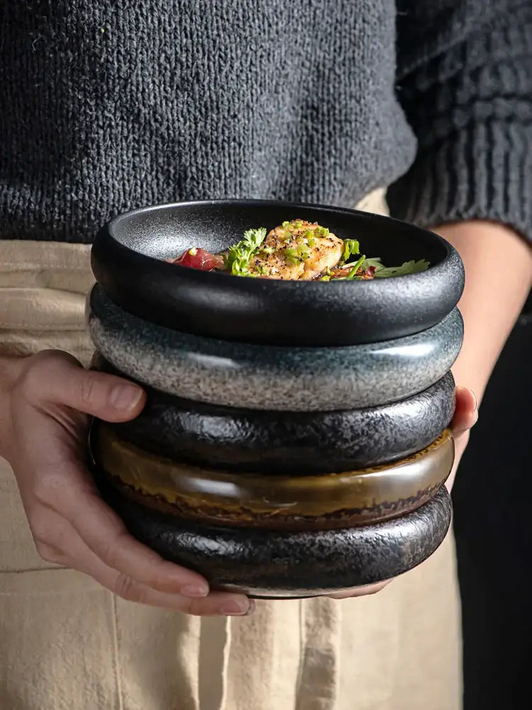 Stack of five rustic ceramic kimchi plates in dark tones with textured handcrafted finish and subtle glaze variations