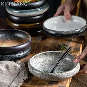 A rustic speckled ceramic kimchi plate with a glossy black rim and white interior for dining use