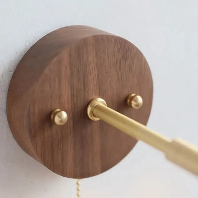 A sleek circular walnut and brass wall light fixture with polished stem and decorative finials for bedroom use